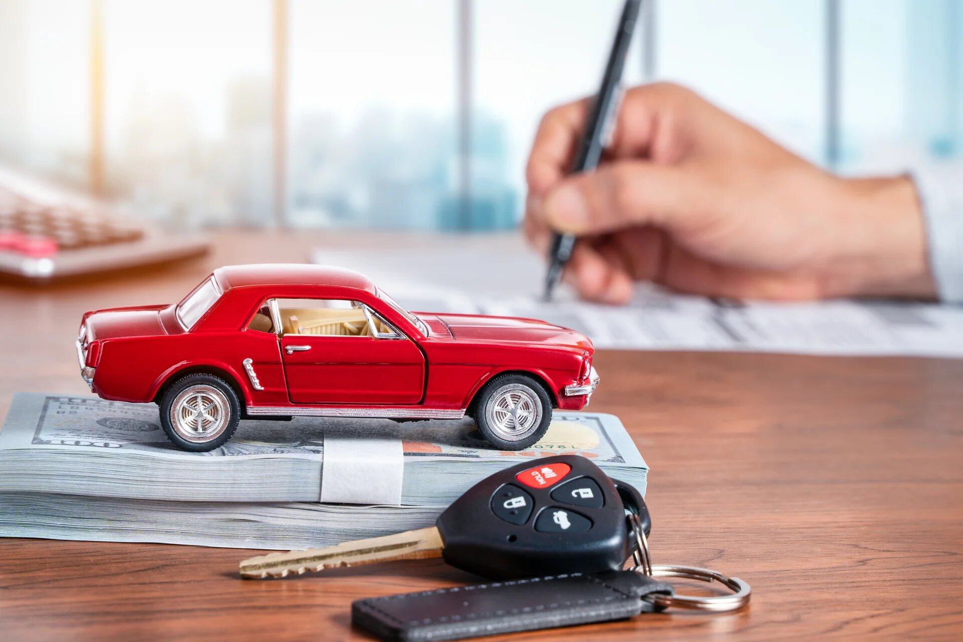 maquette d'une voiture rouge sur une pile de billet et une main qui signe un contrat en arrière plan