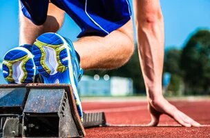 bas du corps d'un athlète avec basket et shorts bleus dans les starting block