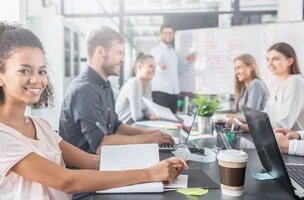 jeune femme qui regarde l'objectif en souriant avec 6 collègues en open space en arrière plan